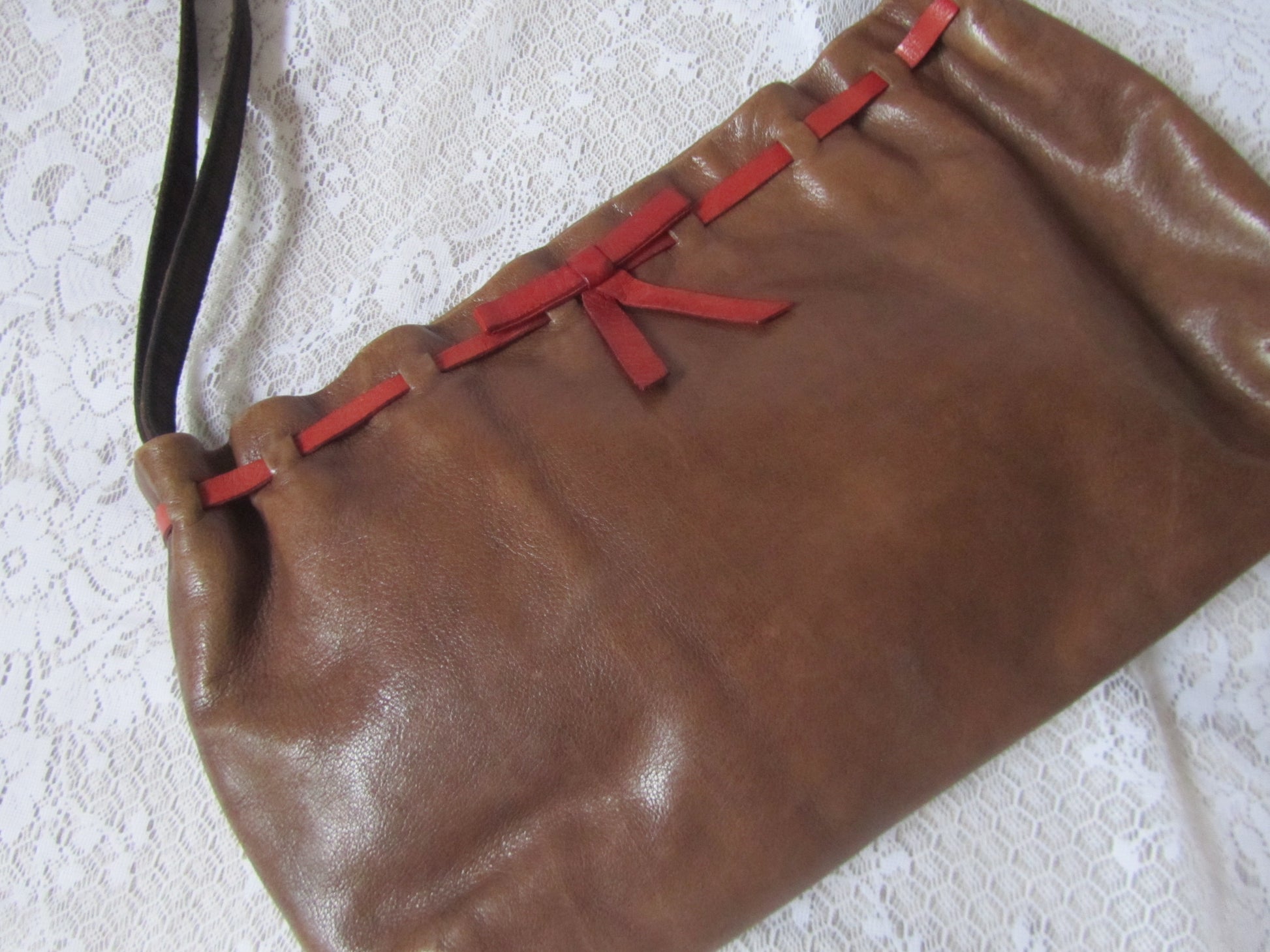 Brown leather clutch with red accents on a textured white surface