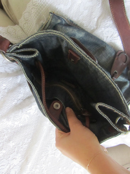 Hand holding a denim bag with leather accents on a white surface