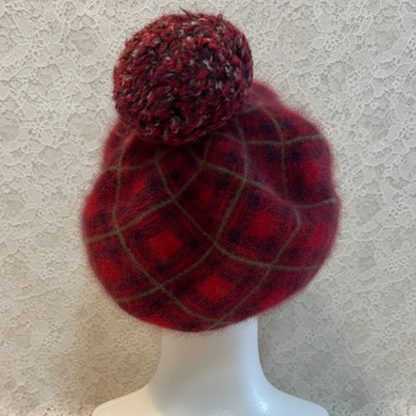 Red plaid beanie with a pom-pom on a mannequin head against a textured wall.