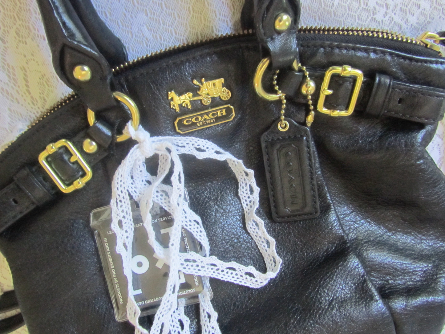 Black leather Coach bag with gold hardware and a lace detail on a textured surface.