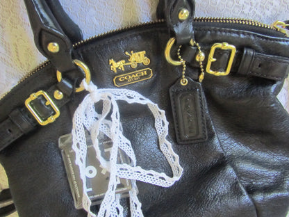 Black leather Coach bag with gold hardware and a lace detail on a textured surface.