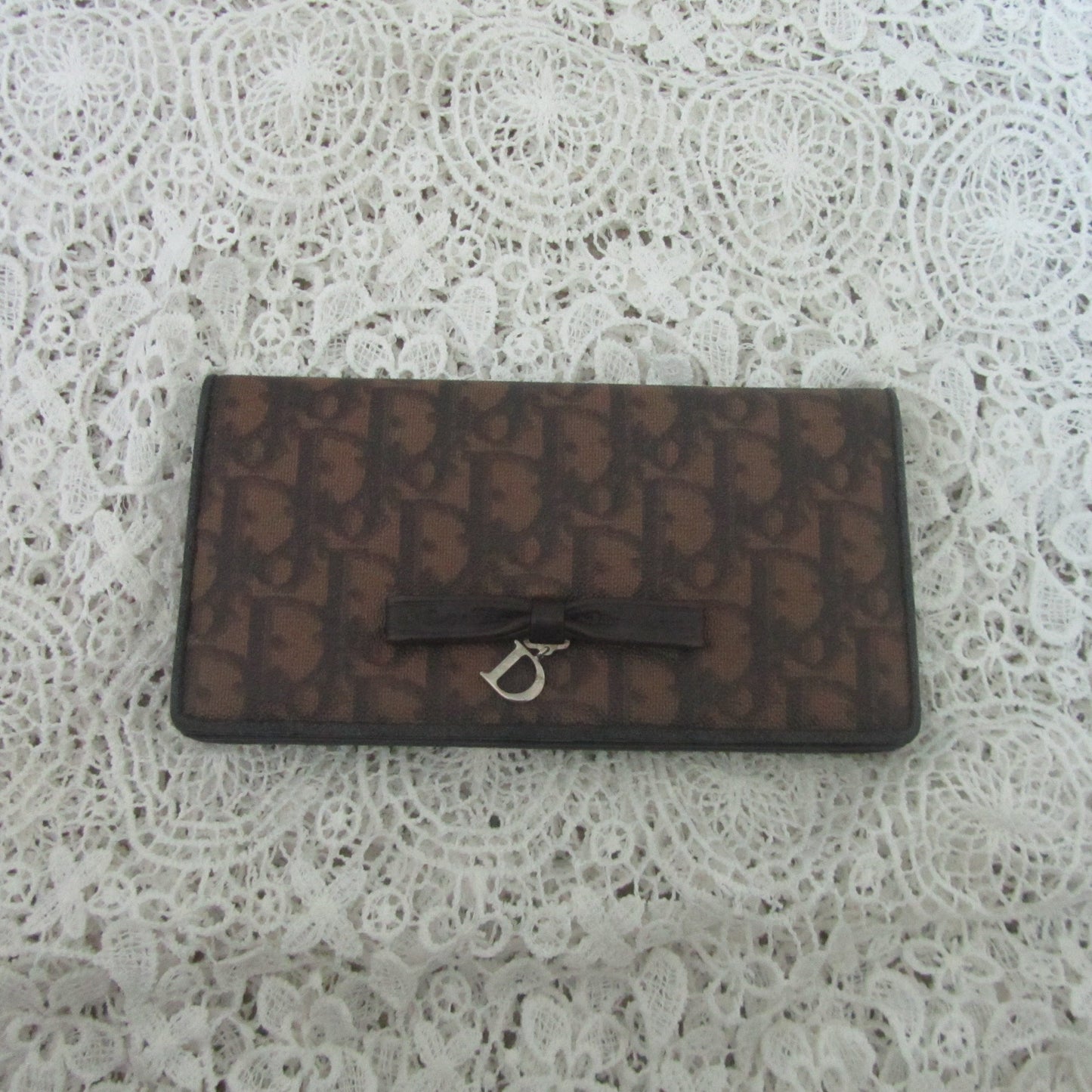 Brown textured wallet with a silver D clasp on a white lace background