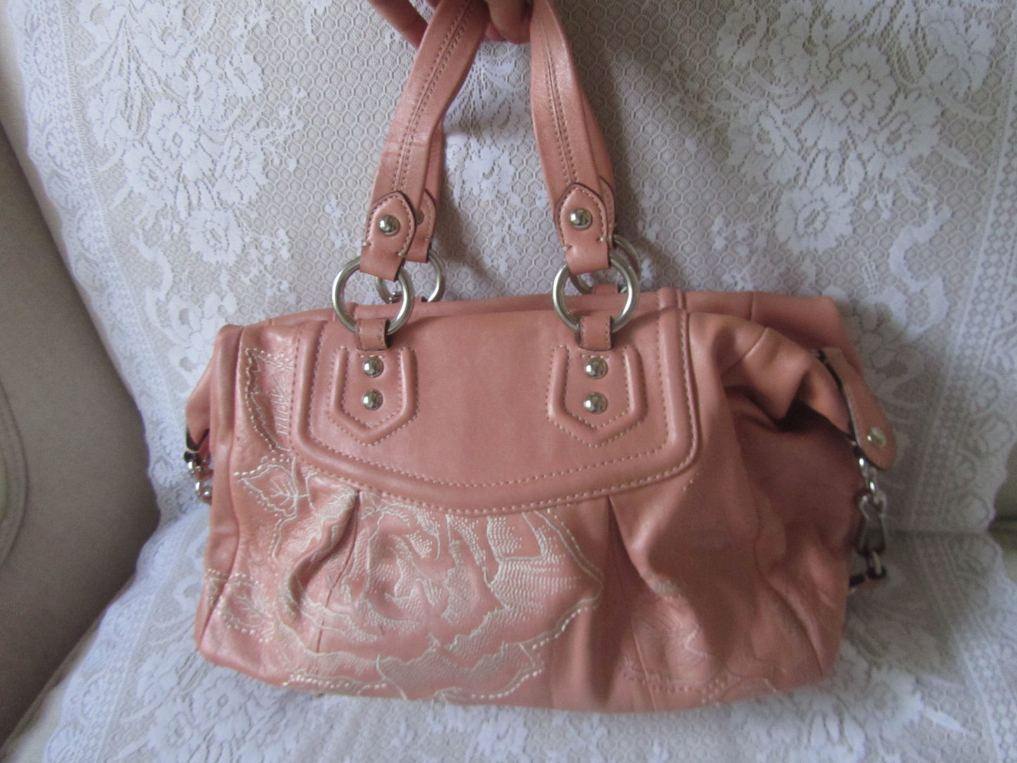 Pink handbag with lace detailing on a textured white surface
