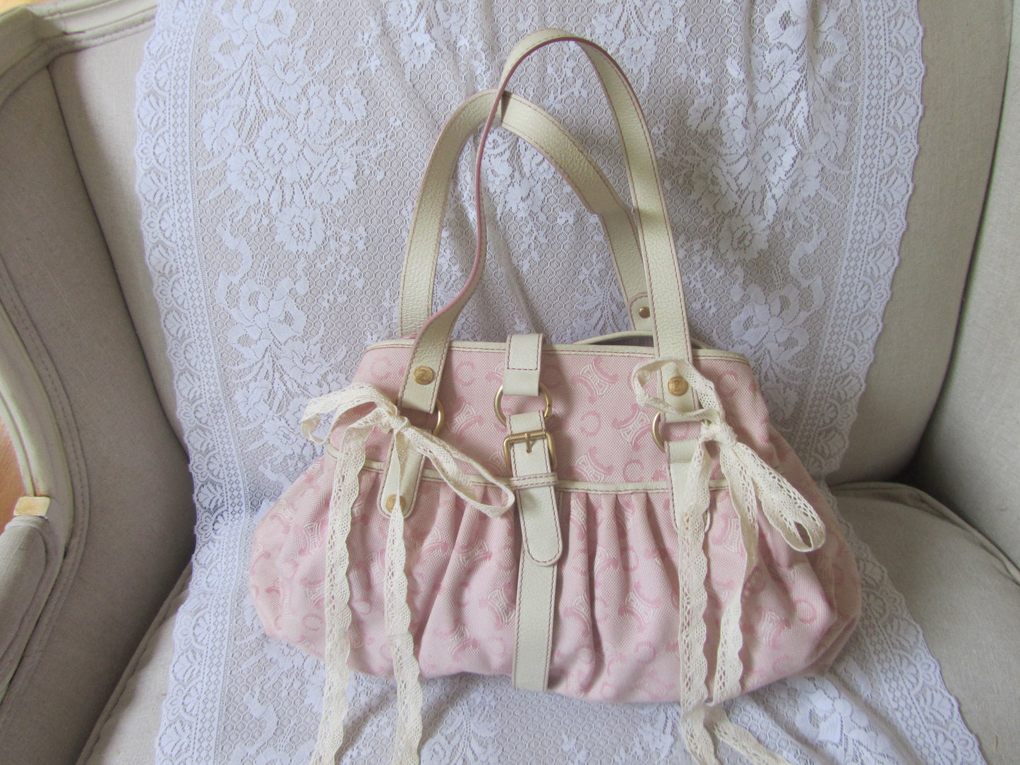 Pink textured handbag with beige straps on a lace-covered surface