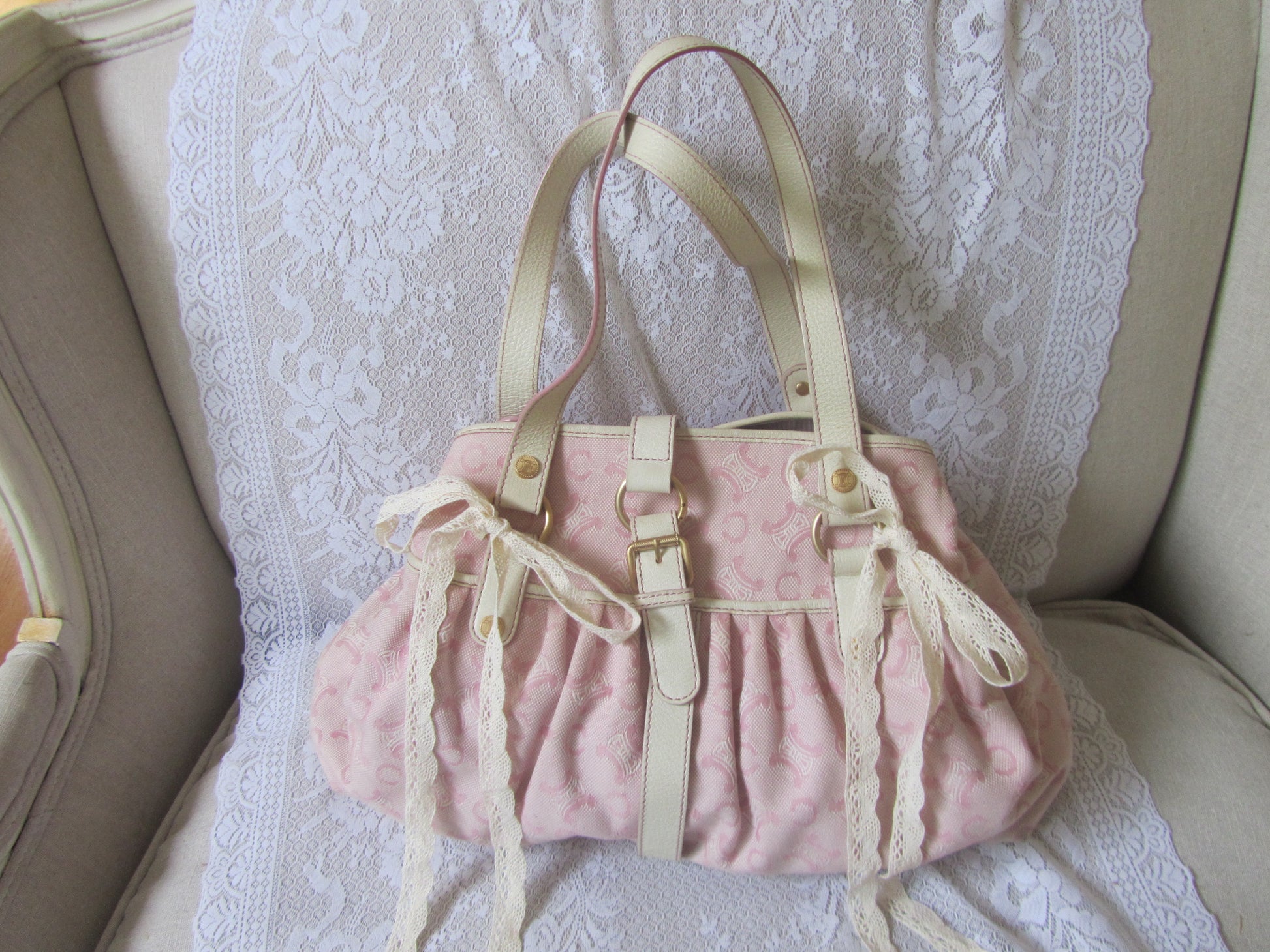 Pink textured handbag with beige straps on a lace-covered surface