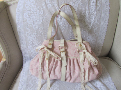 Pink textured handbag with beige straps on a lace-covered surface