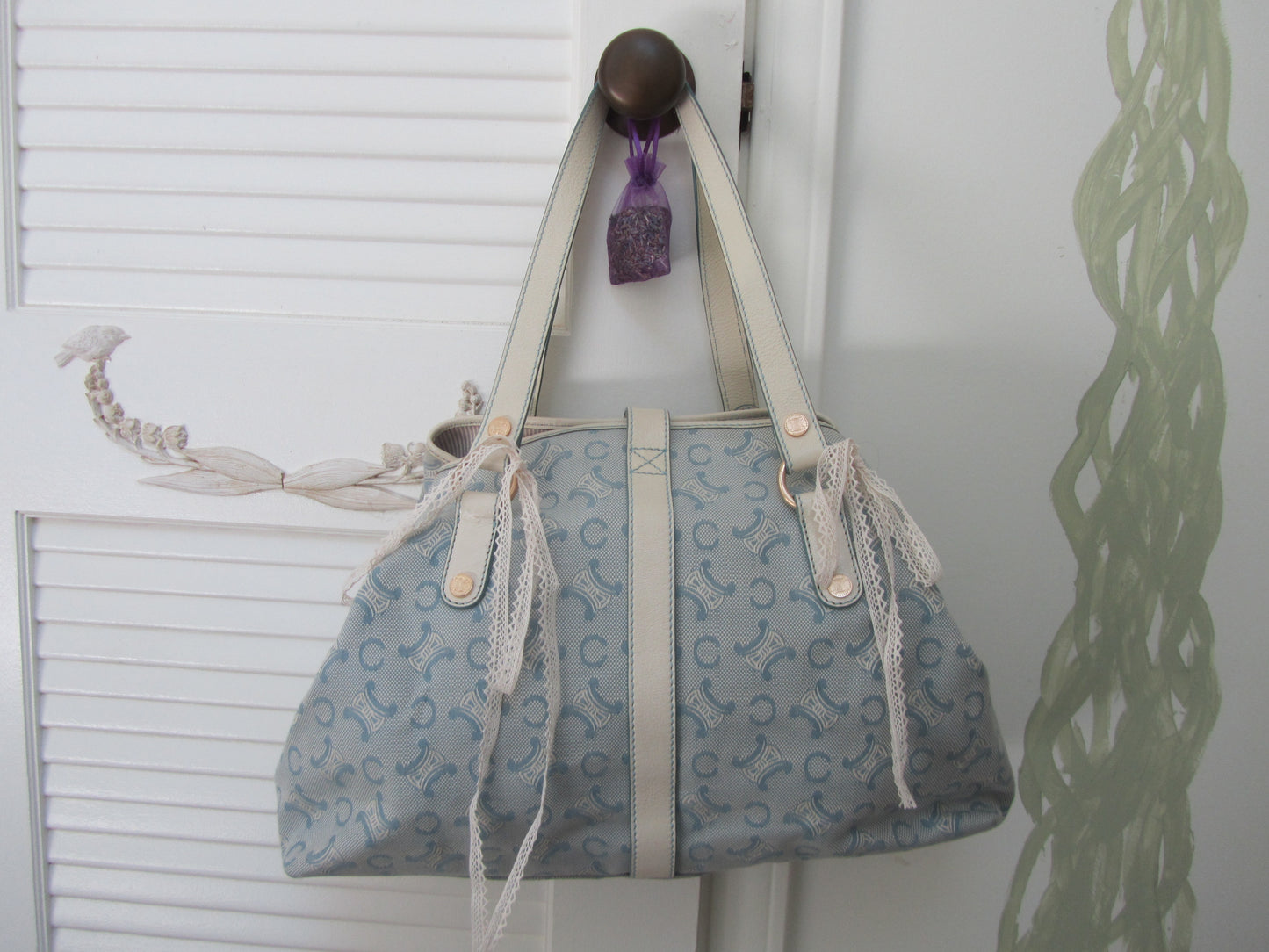 Blue handbag with white pattern hanging on a hook against a white wall.