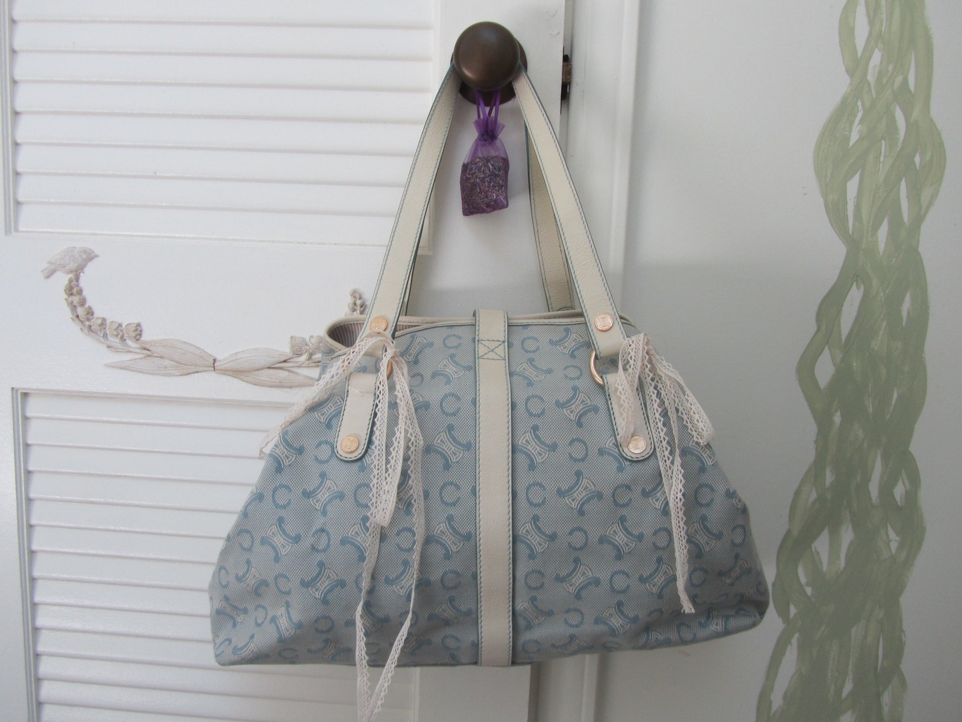 Blue handbag with white pattern hanging on a hook against a white wall.