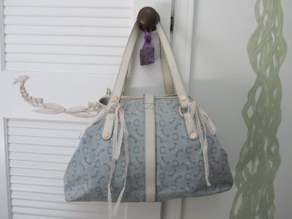 Blue handbag with white pattern hanging on a hook against a white wall.