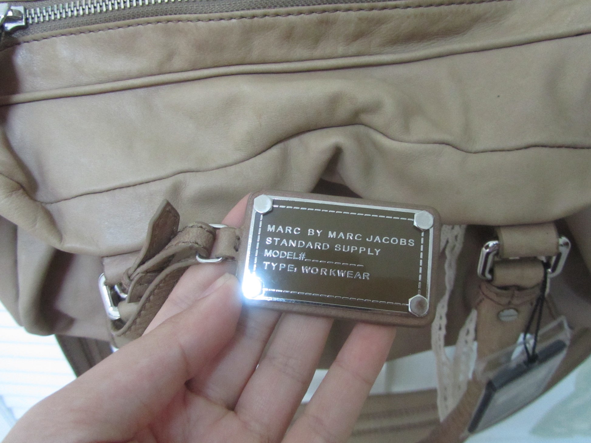 Beige leather bag with a brand label held by a hand