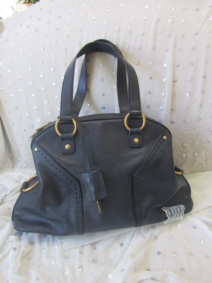 Black leather handbag with gold hardware on a textured white surface