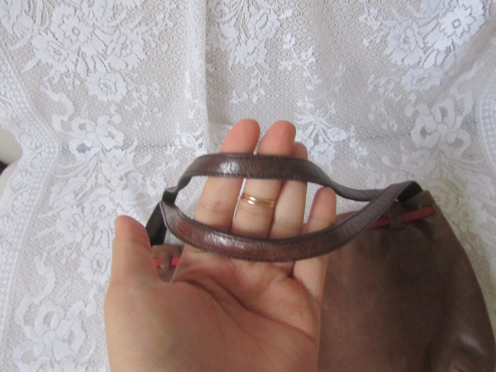 Hand holding a brown leather strap against a textured white background