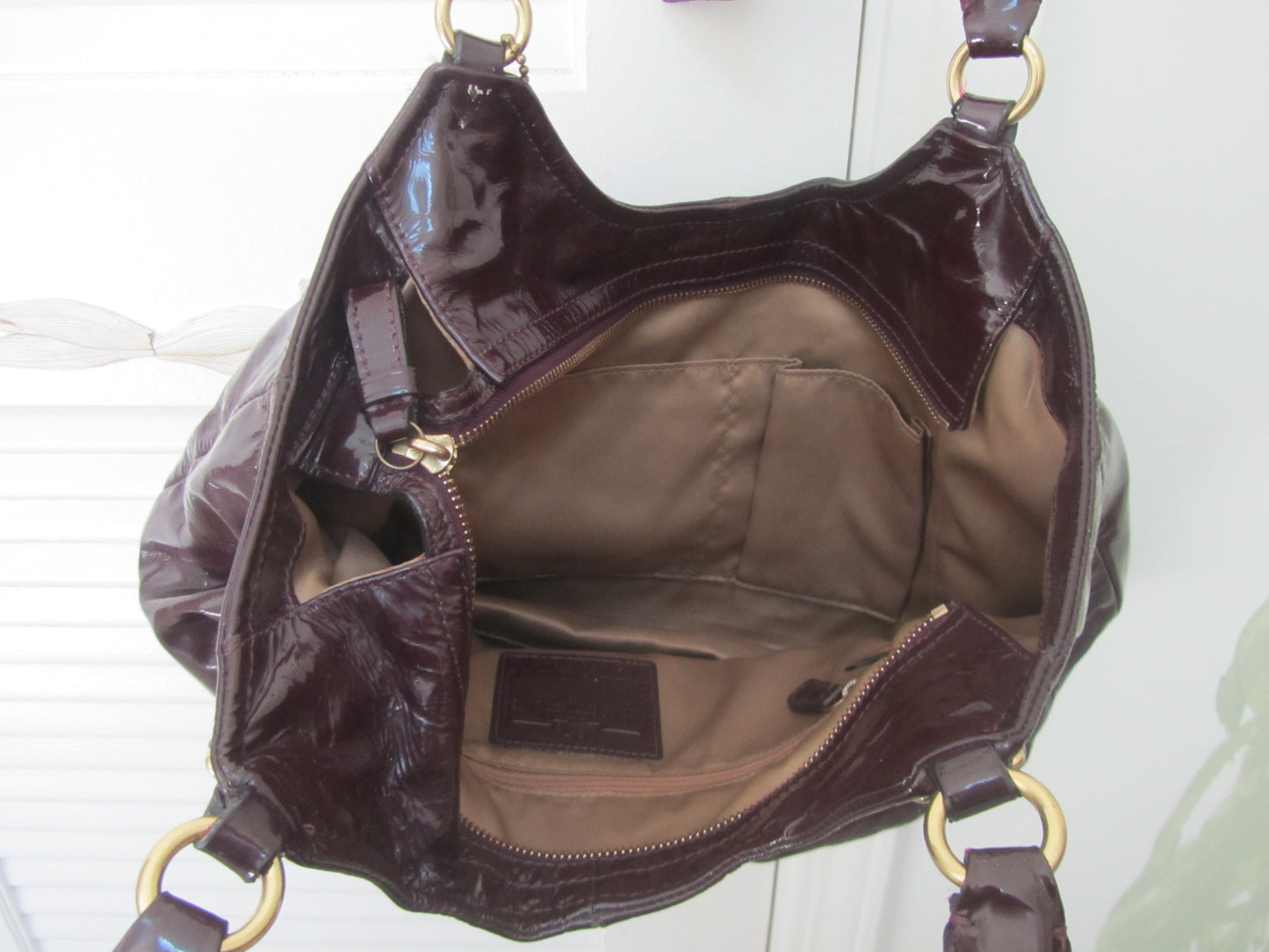 Brown patent leather handbag with gold hardware on a white background