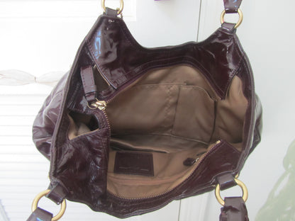 Brown patent leather handbag with gold hardware on a white background