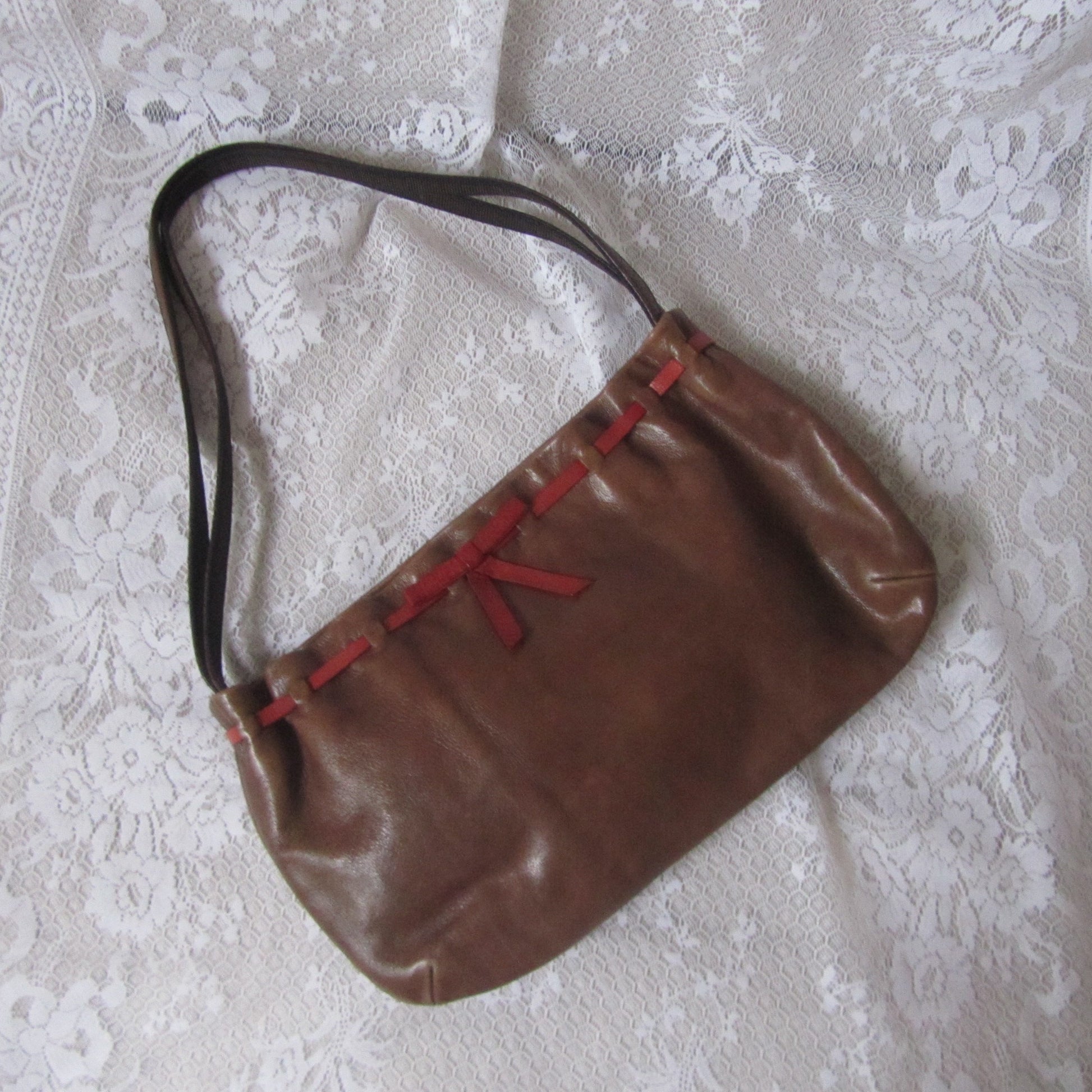 Brown handbag with red accents on a white lace tablecloth