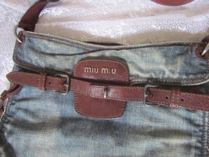 Close-up of a denim bag with a brown leather strap featuring 'miu miu' branding.