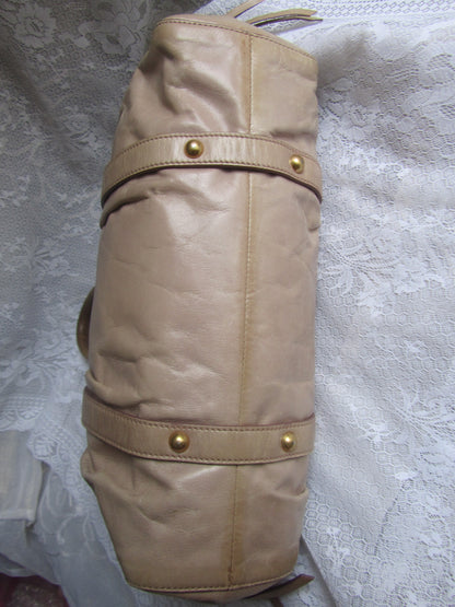 Beige leather bag with gold buttons on a textured gray background