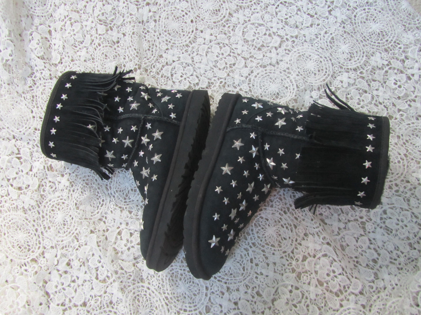 Black boots with white star patterns and fringes on a textured surface