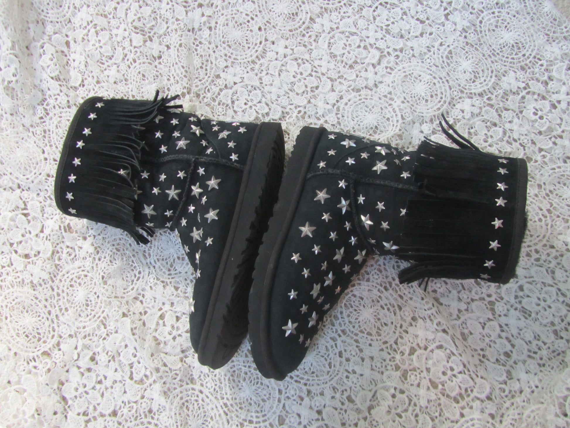 Black boots with white star patterns and fringes on a textured surface