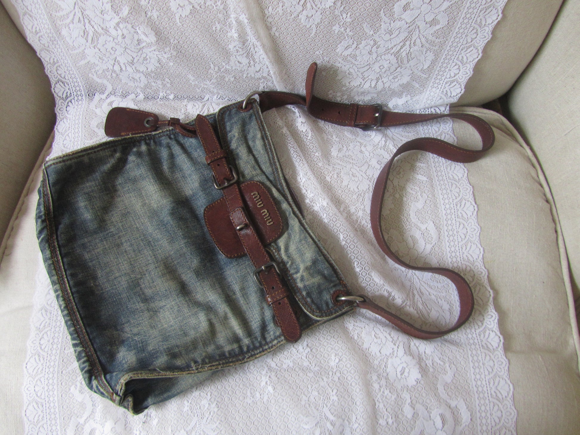 Denim bag with brown straps on a white lace fabric background