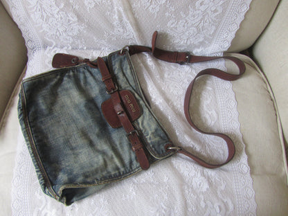 Denim bag with brown straps on a white lace fabric background