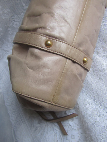 Close-up of a beige leather bag with gold studs on a textured white background
