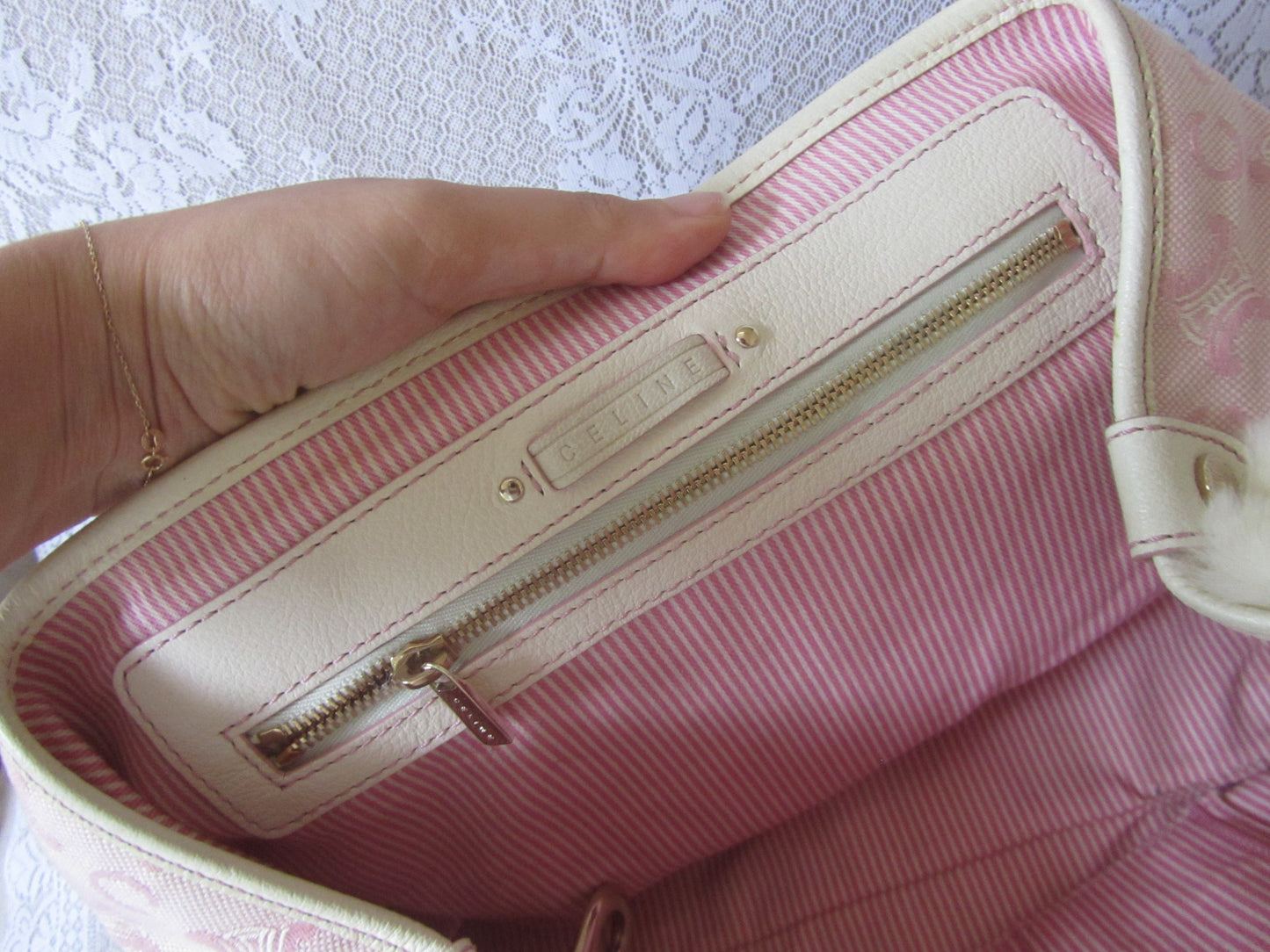 Pink handbag with a gold zipper being held by a hand on a textured white background