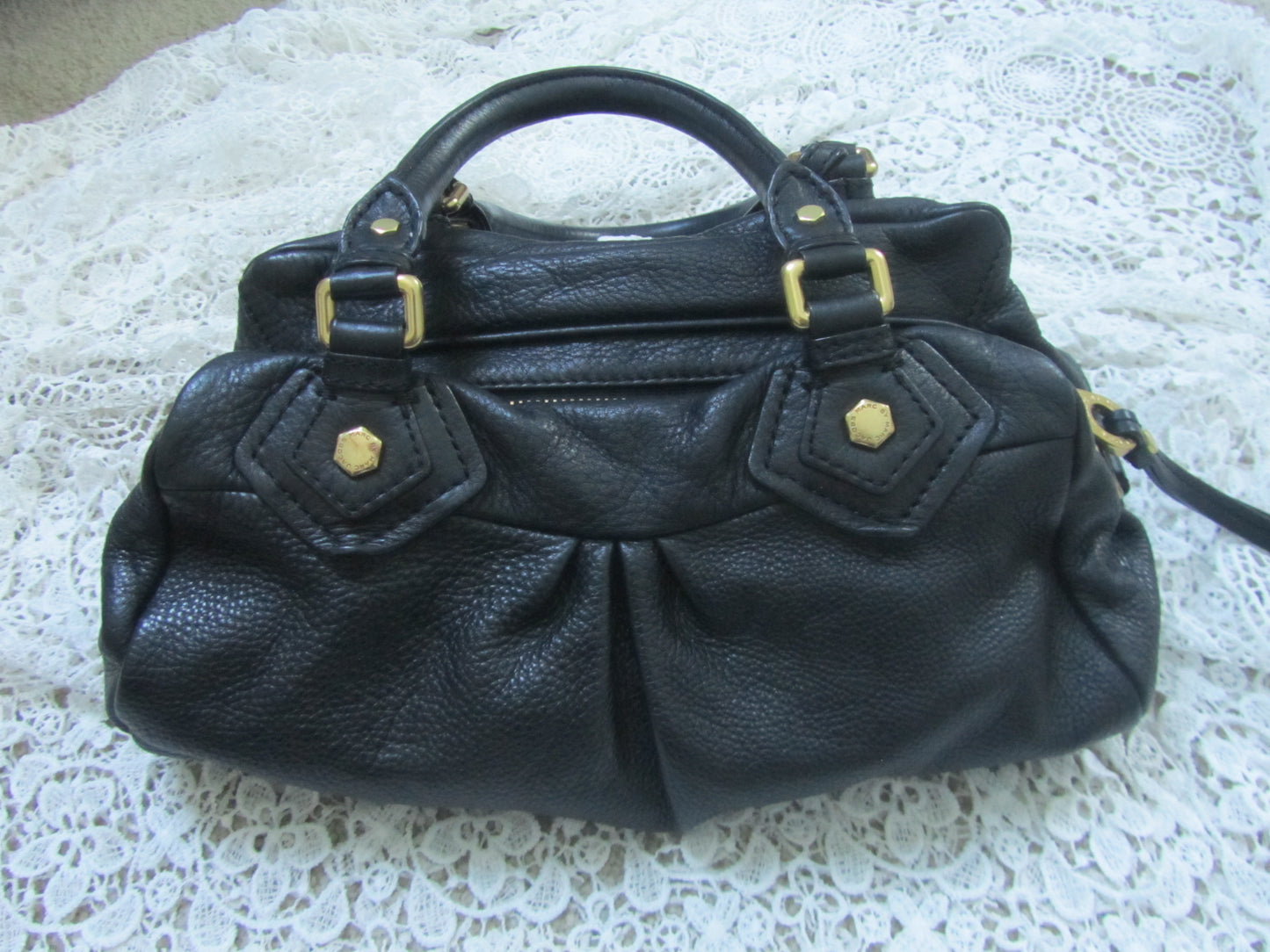 Black leather handbag with gold accents on a textured white surface