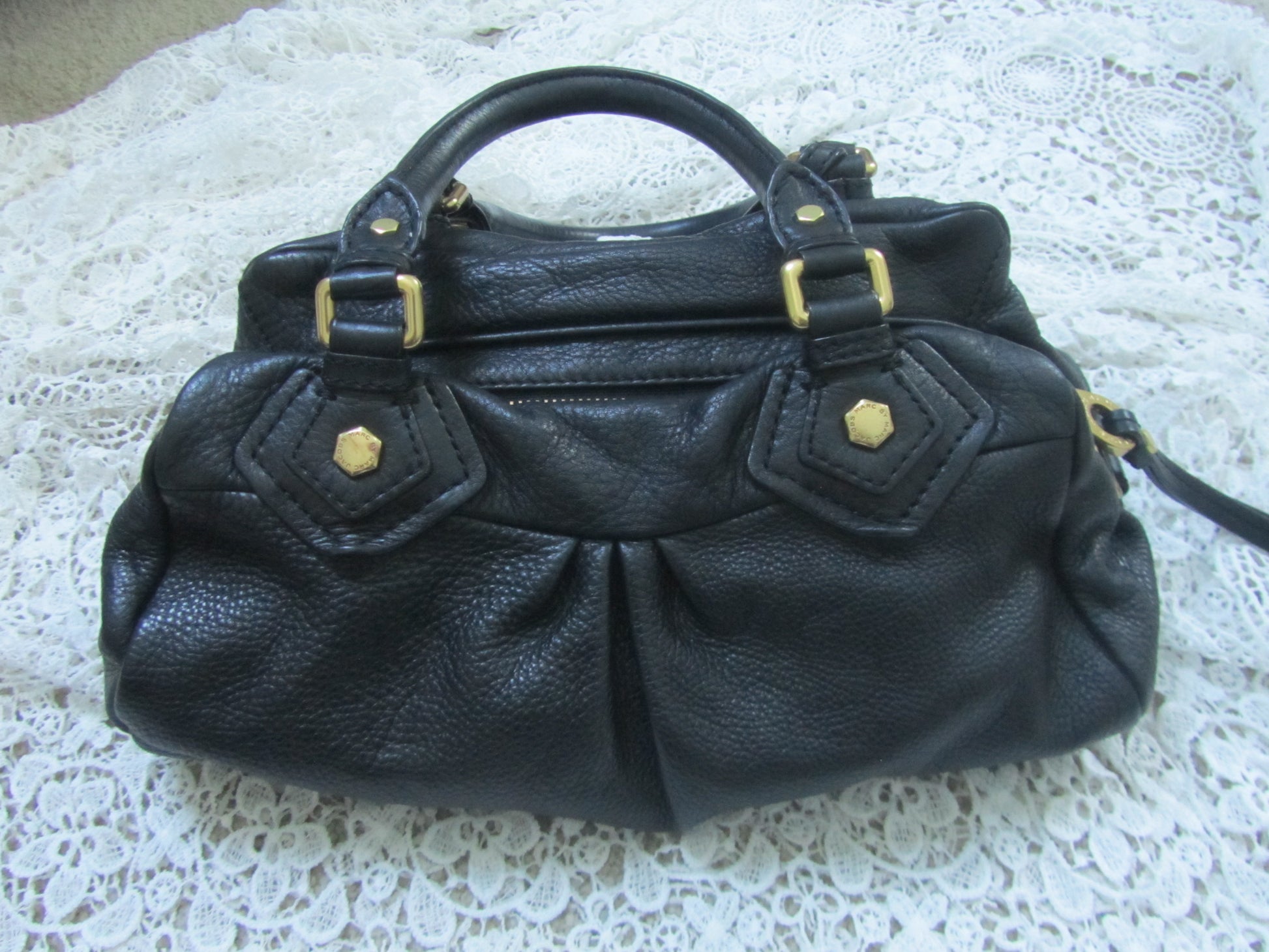 Black leather handbag with gold accents on a textured white surface