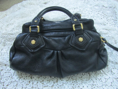 Black leather handbag with gold accents on a textured white surface