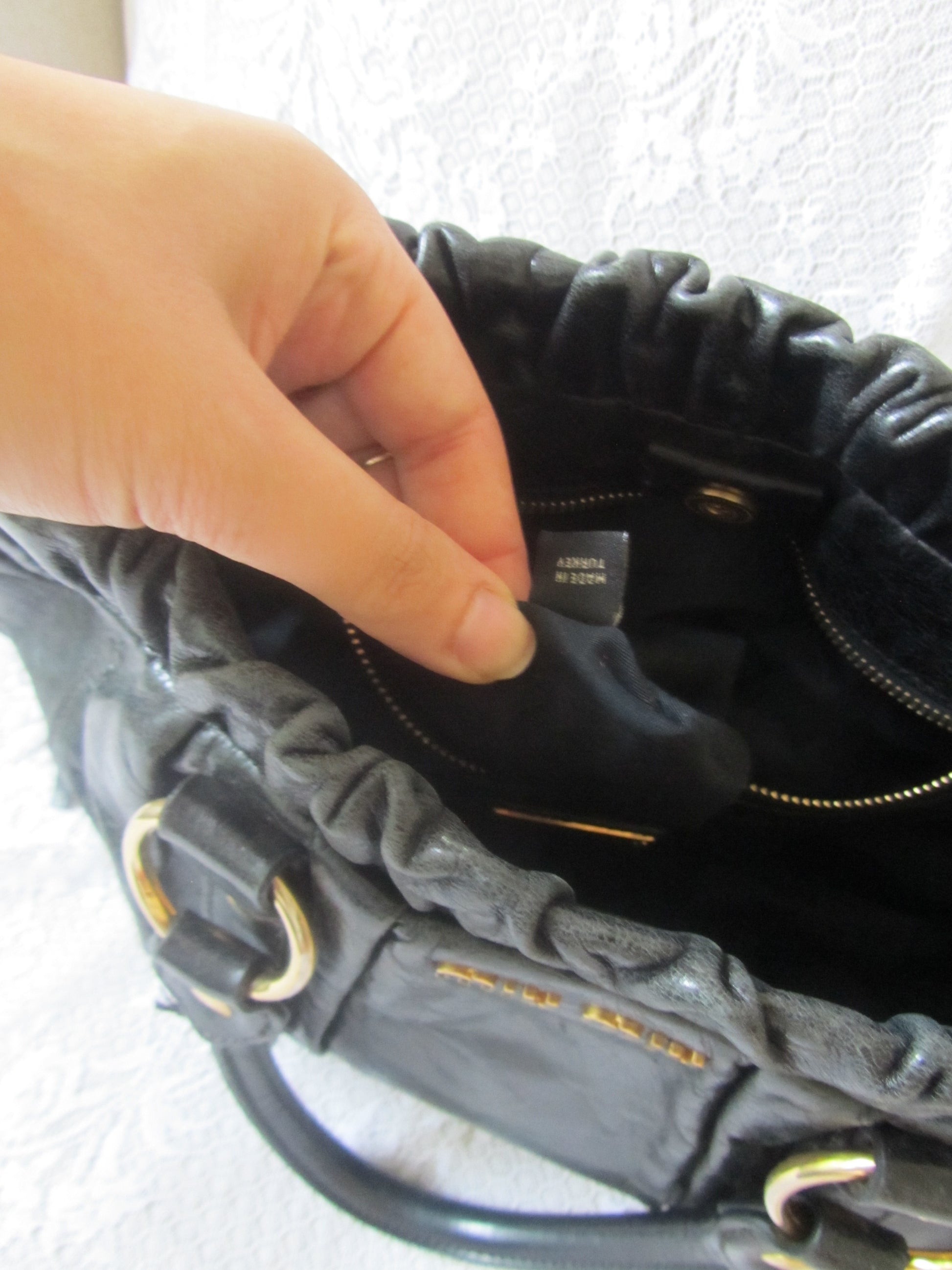 Close-up of a hand holding a black leather bag with a visible brand label.