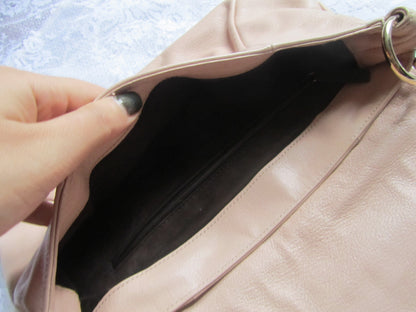Close-up of a beige handbag with a hand holding it open, showing the interior.