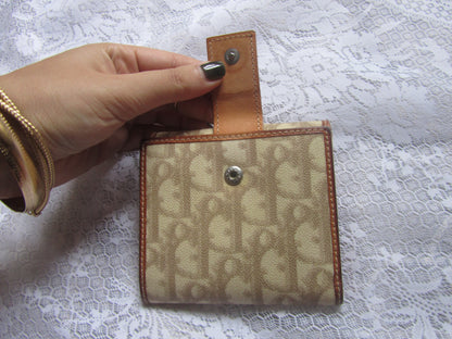 Hand holding a small beige and brown patterned wallet on a white lace background