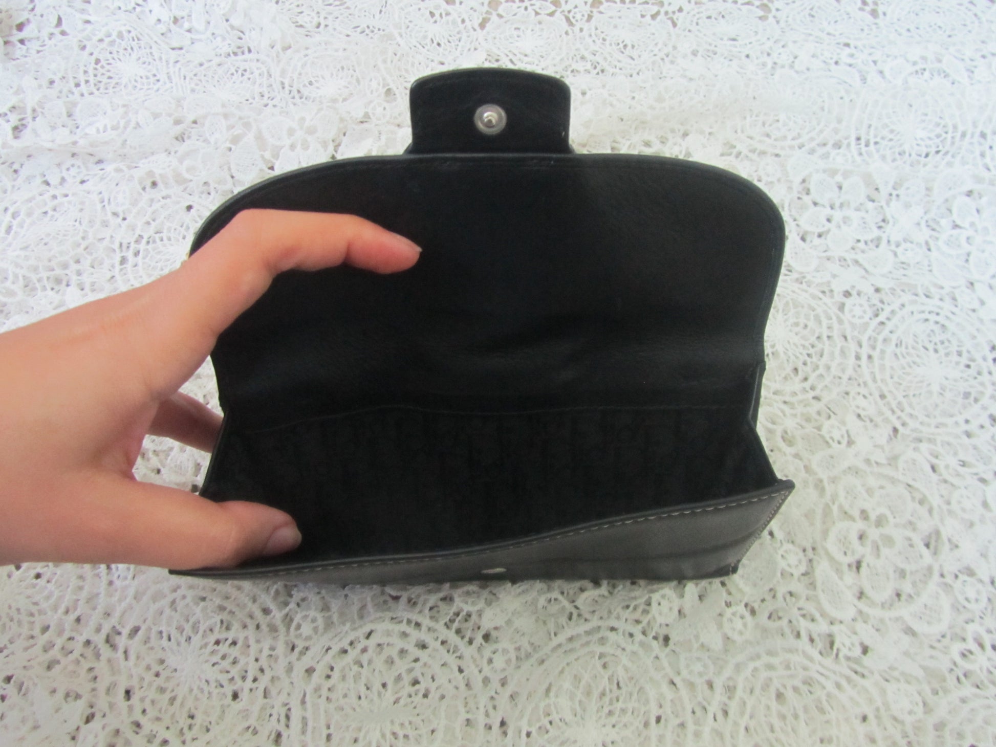 Black clutch bag held by a hand on a textured white surface