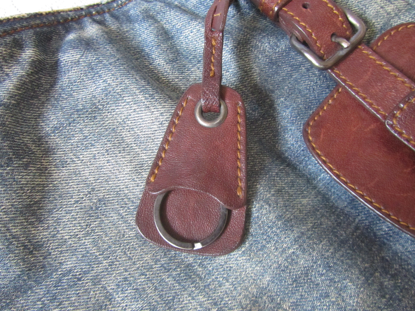 Brown leather keychain attached to a blue denim surface