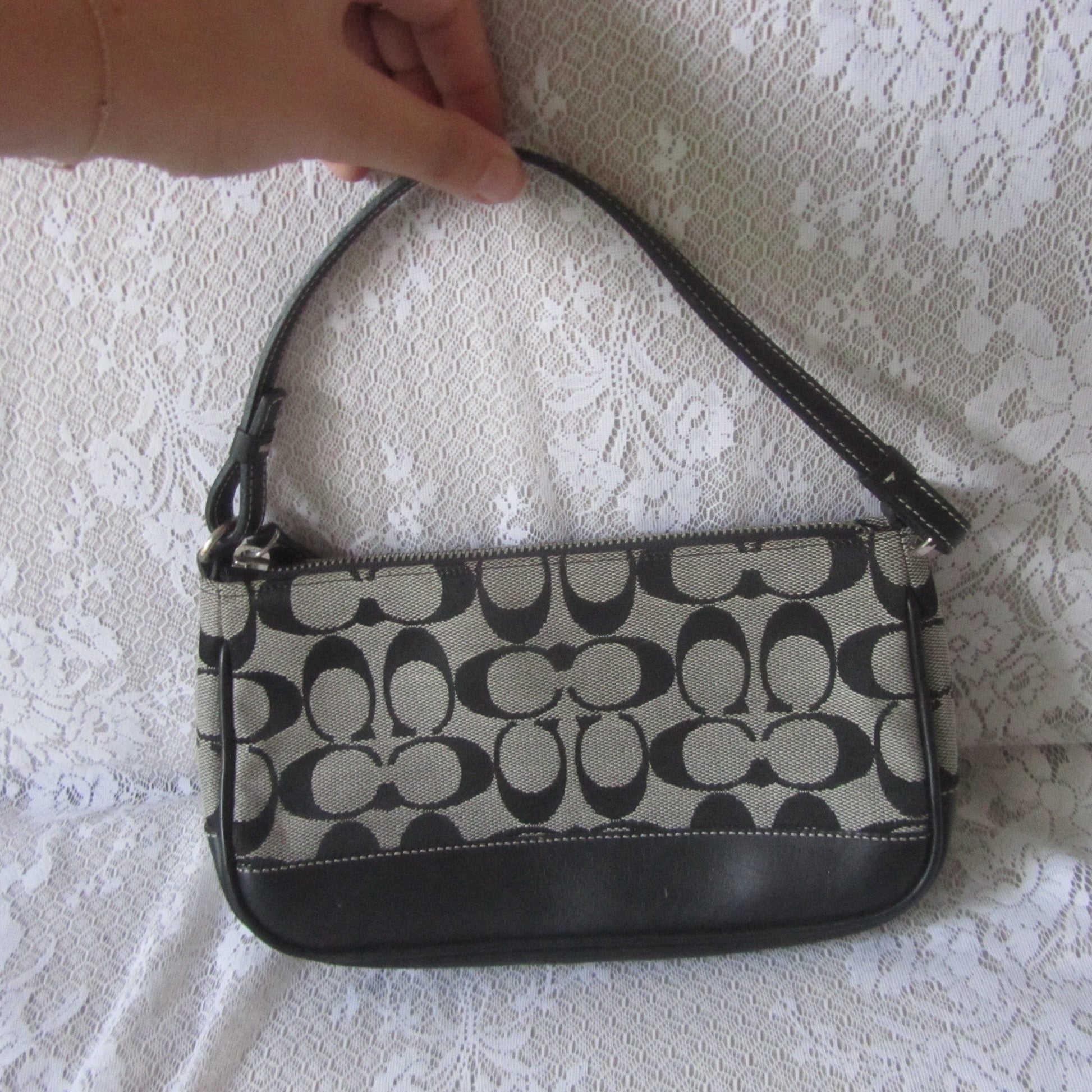 Handbag with black and beige pattern held by a hand on a white lace background