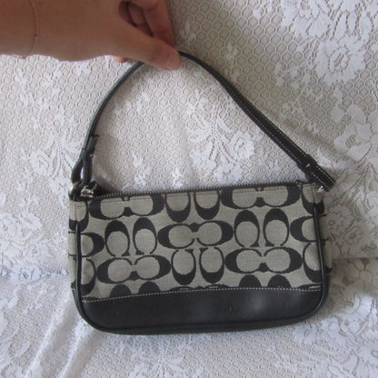 Handbag with black and beige pattern held by a hand on a white lace background