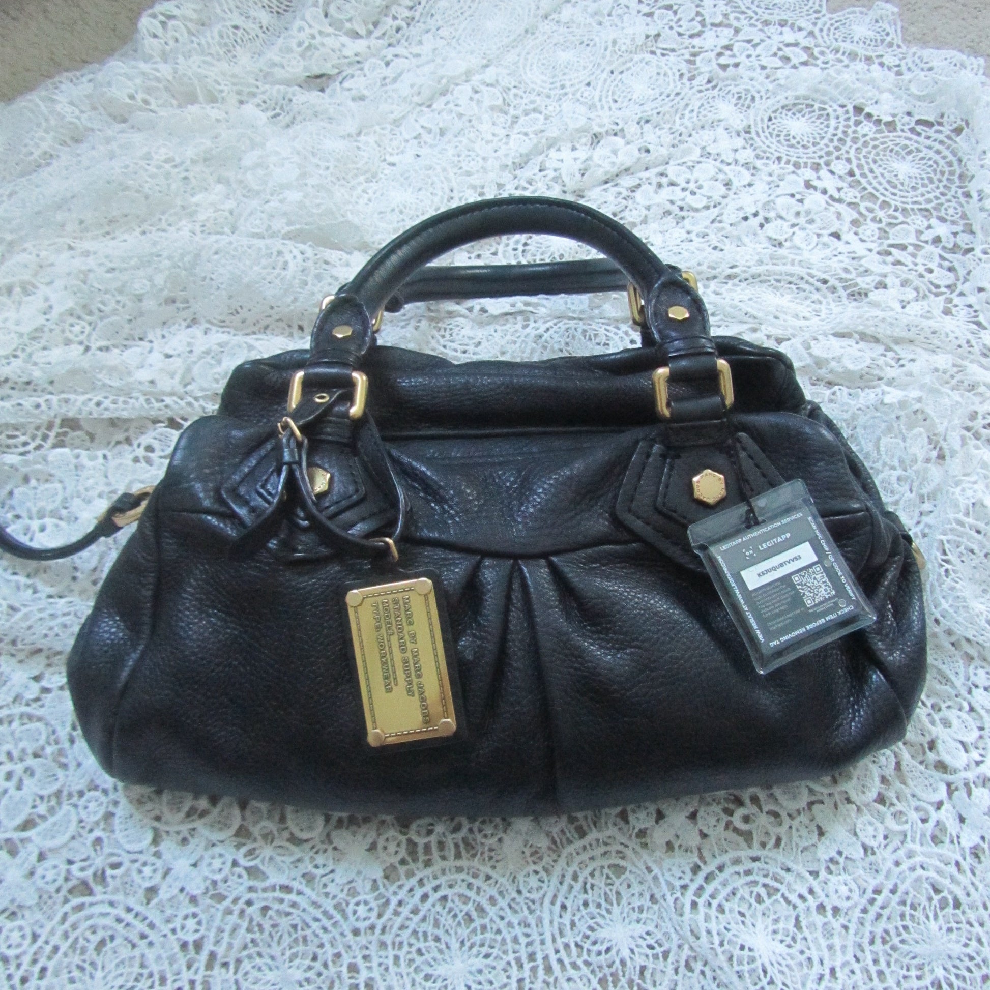 Black handbag with gold tag on a white lace surface