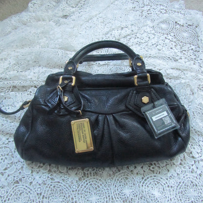 Black handbag with gold tag on a white lace surface