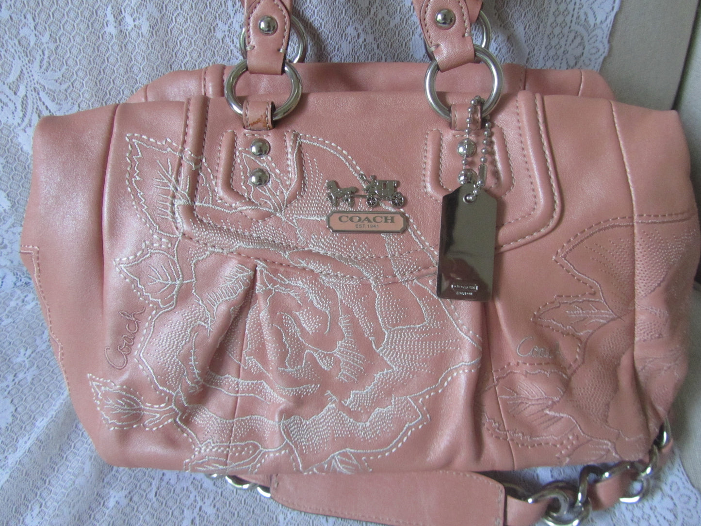 Pink Coach handbag with floral embroidery on a textured surface