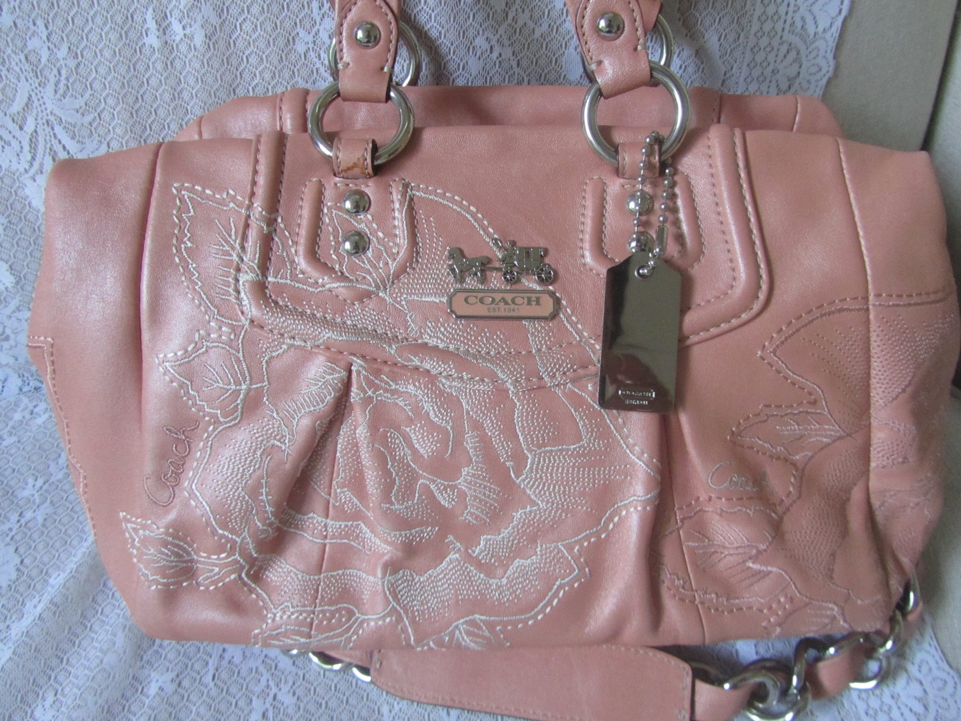 Pink Coach handbag with floral embroidery on a textured surface
