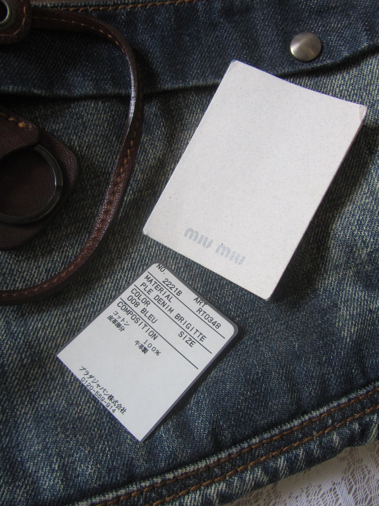 Denim bag with brand labels and a belt on a textured surface