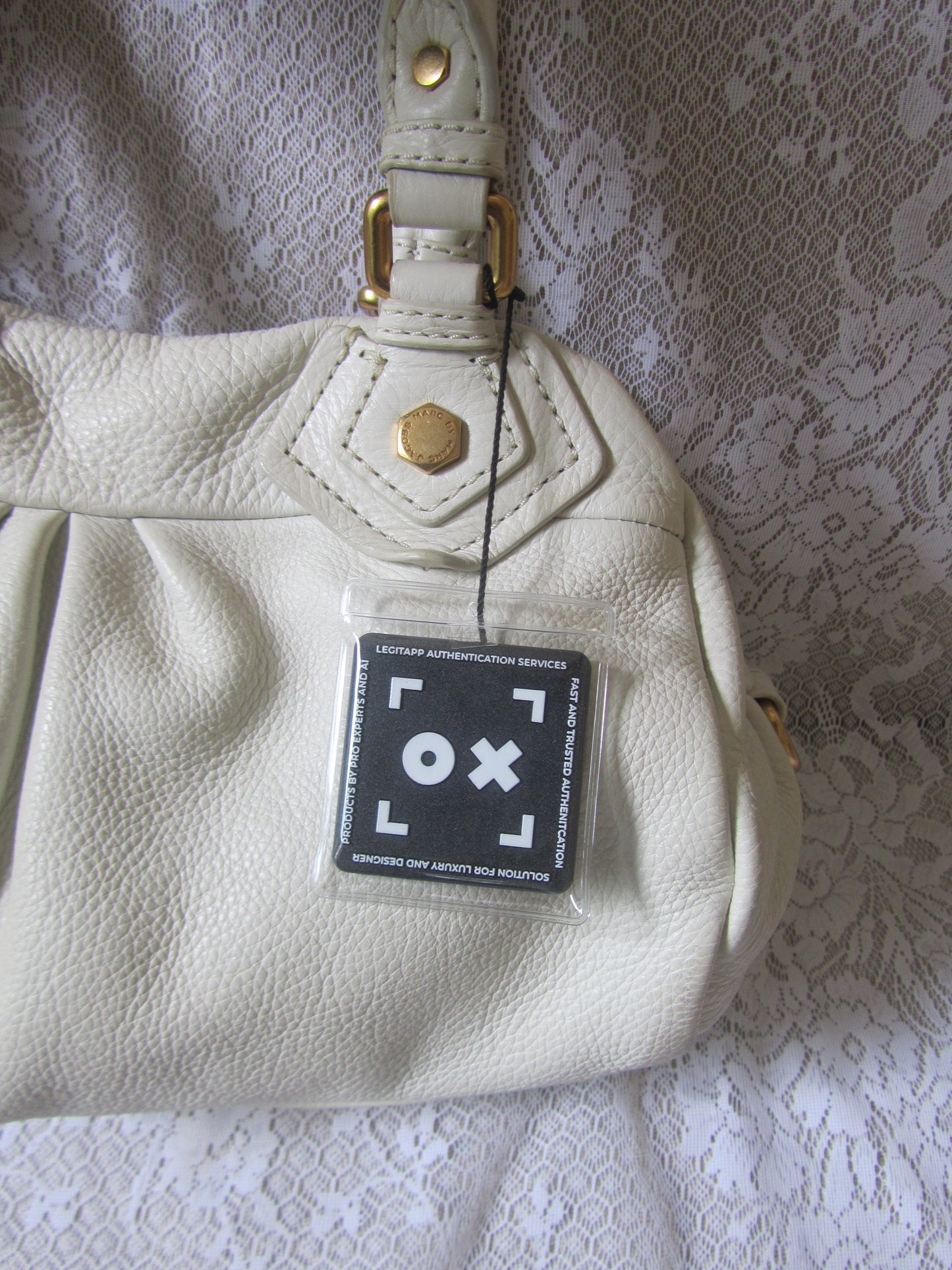 White leather handbag with a brand authenticity tag on a textured gray background