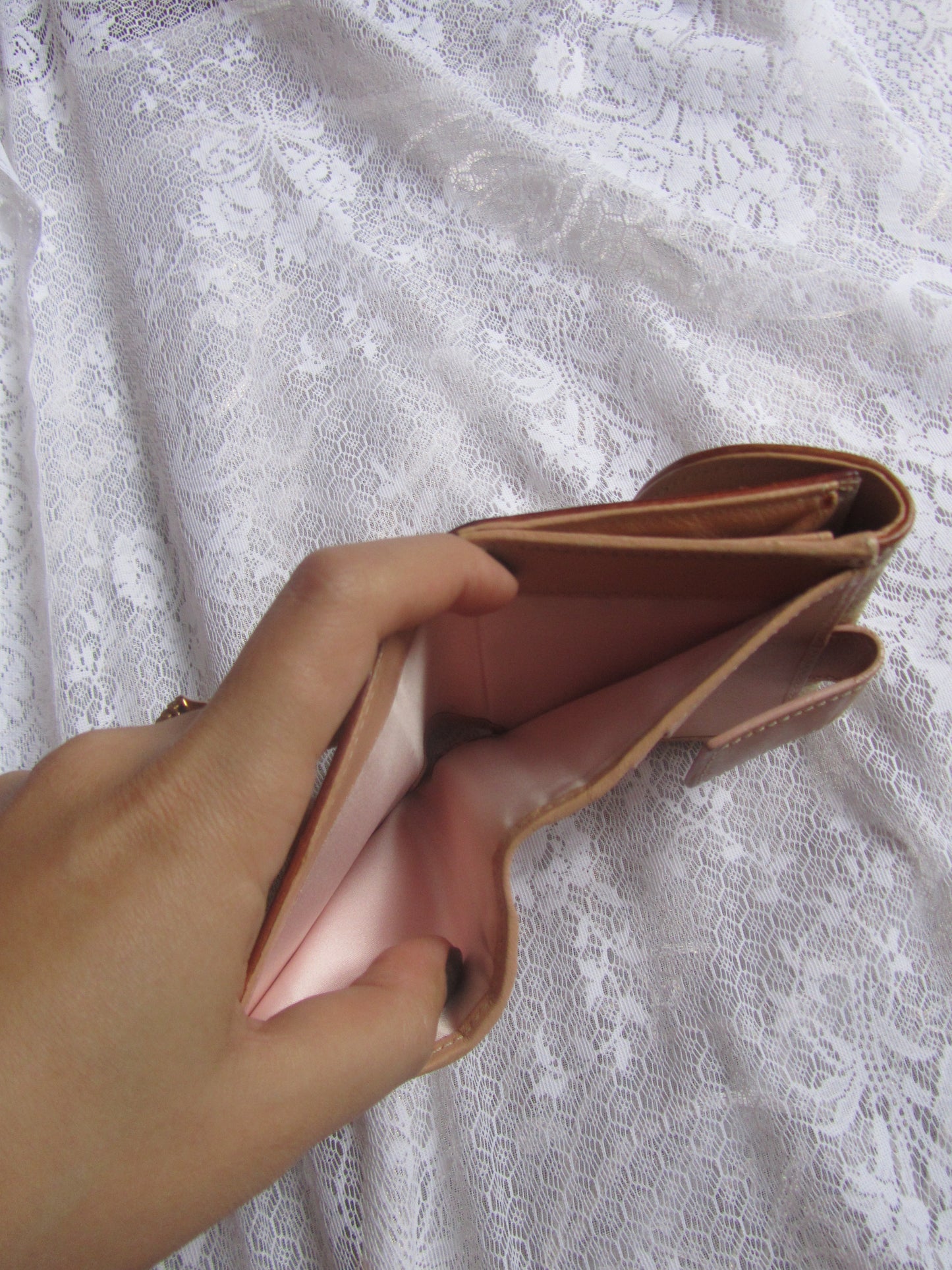 Hand holding a pink wallet against a textured white background