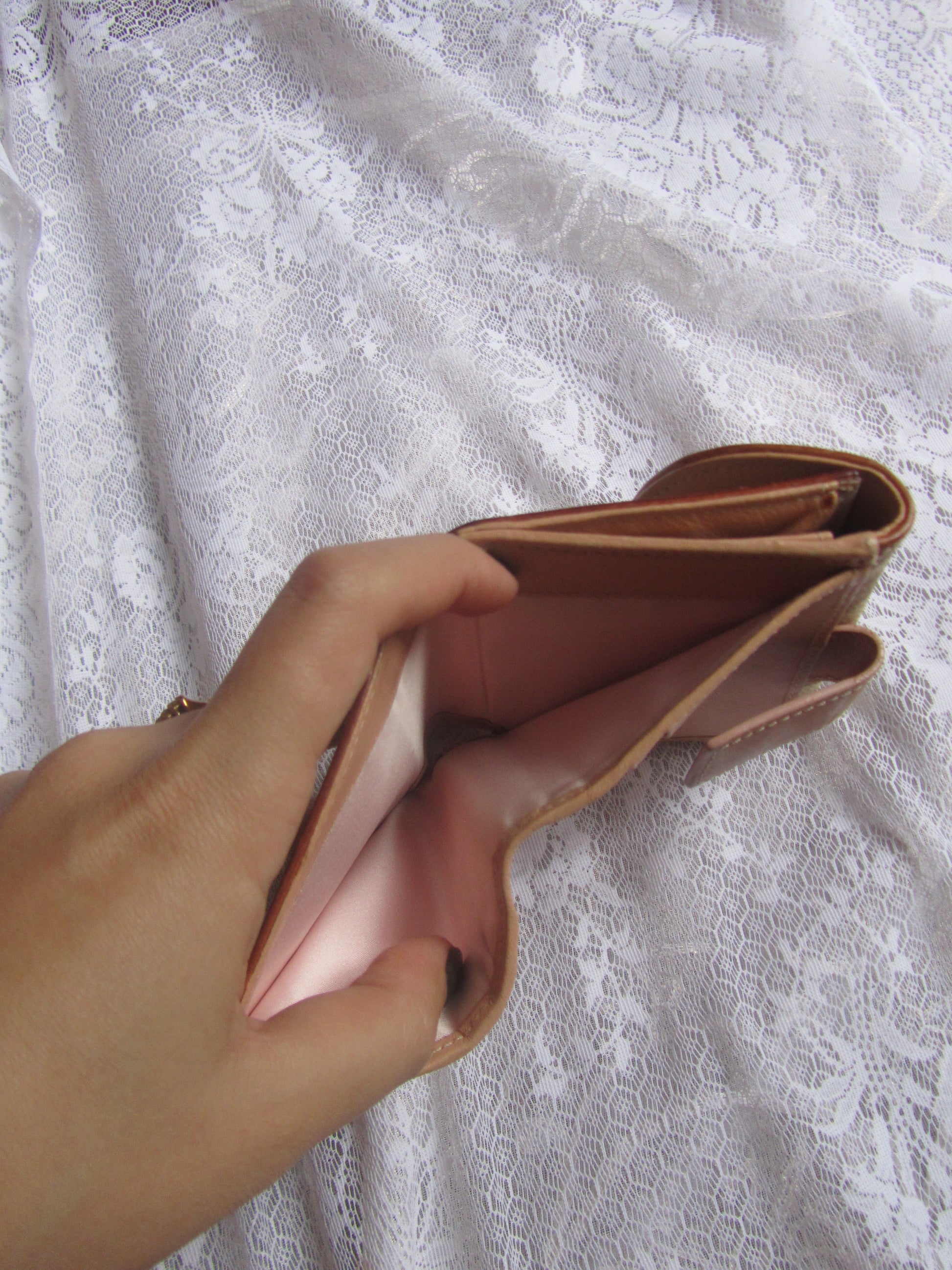 Hand holding a pink wallet against a textured white background