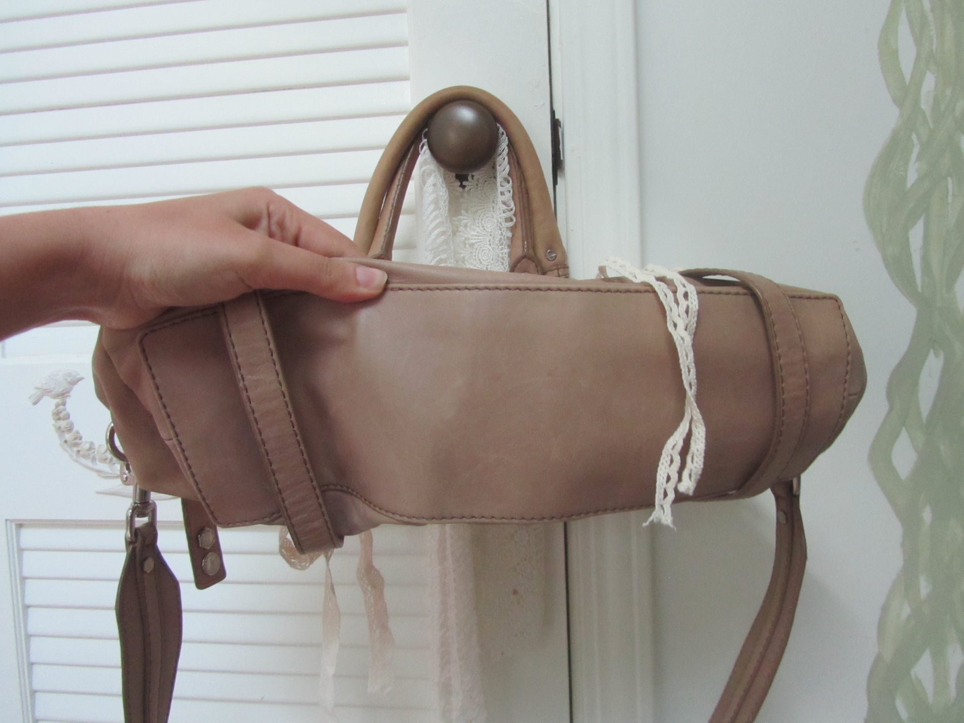 Brown leather handbag held by a hand against a white background