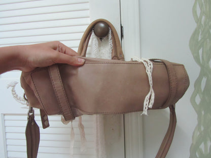Brown leather handbag held by a hand against a white background