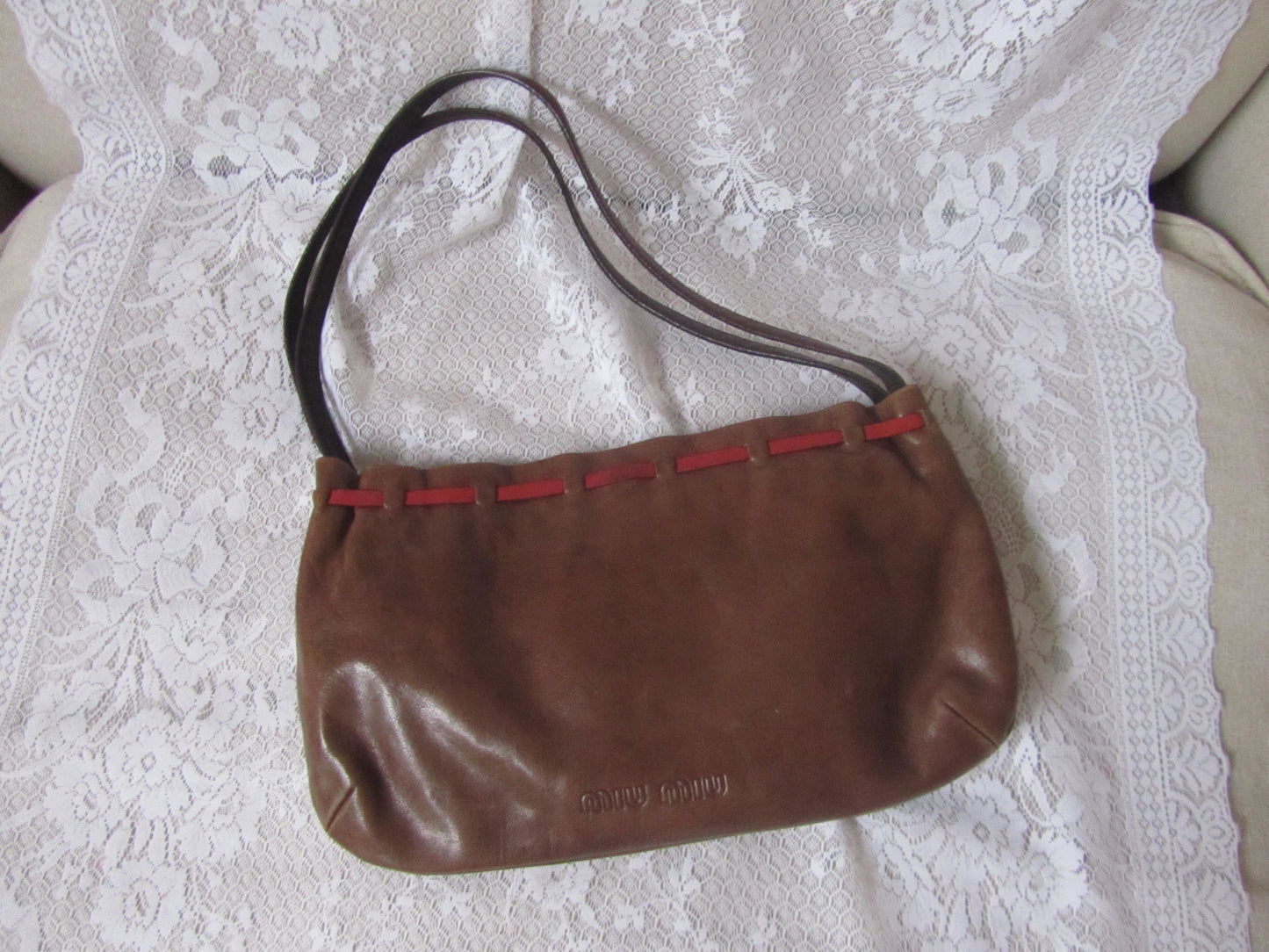 Brown handbag with red accents on a white lace fabric background
