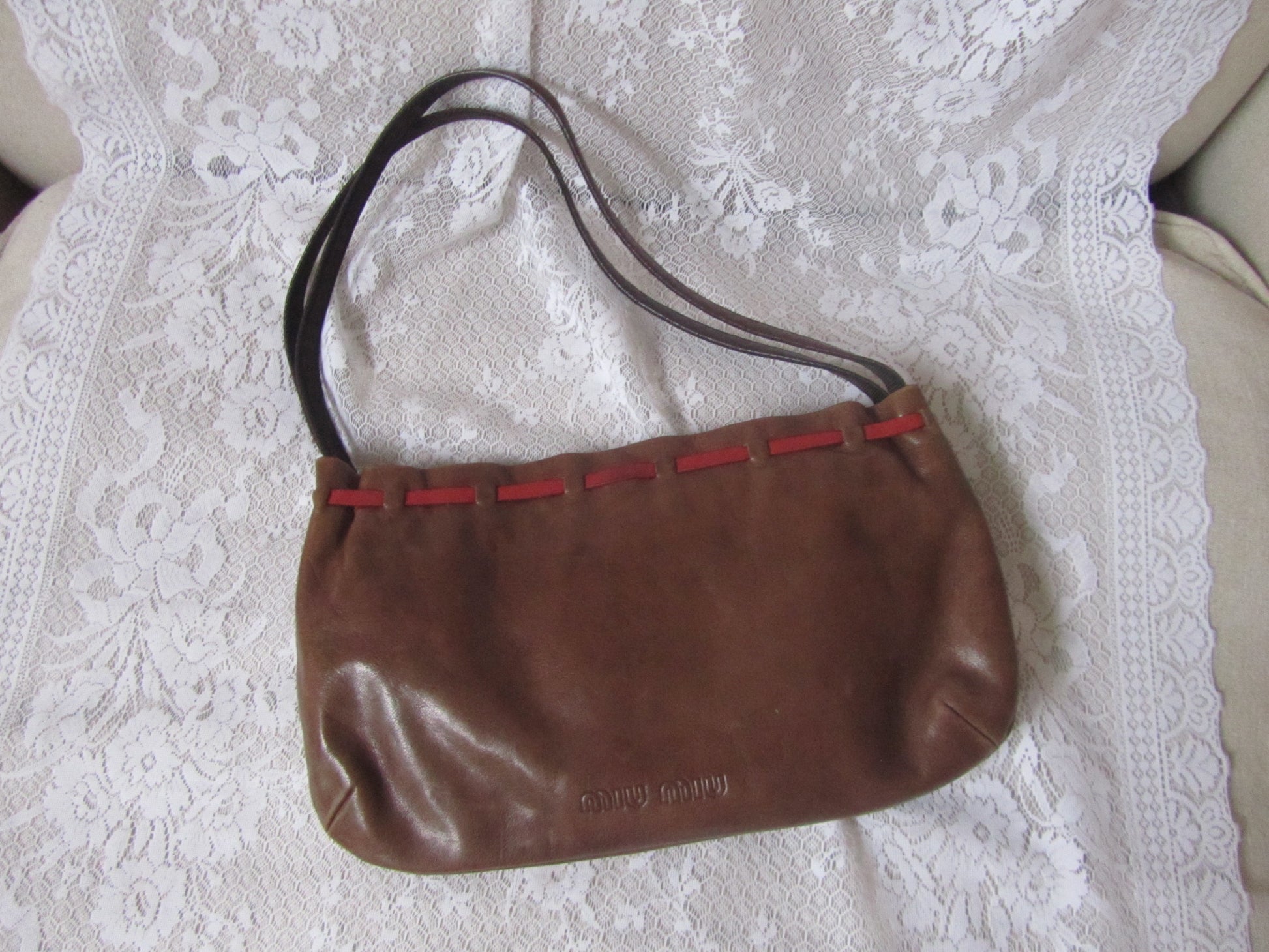 Brown handbag with red accents on a white lace fabric background