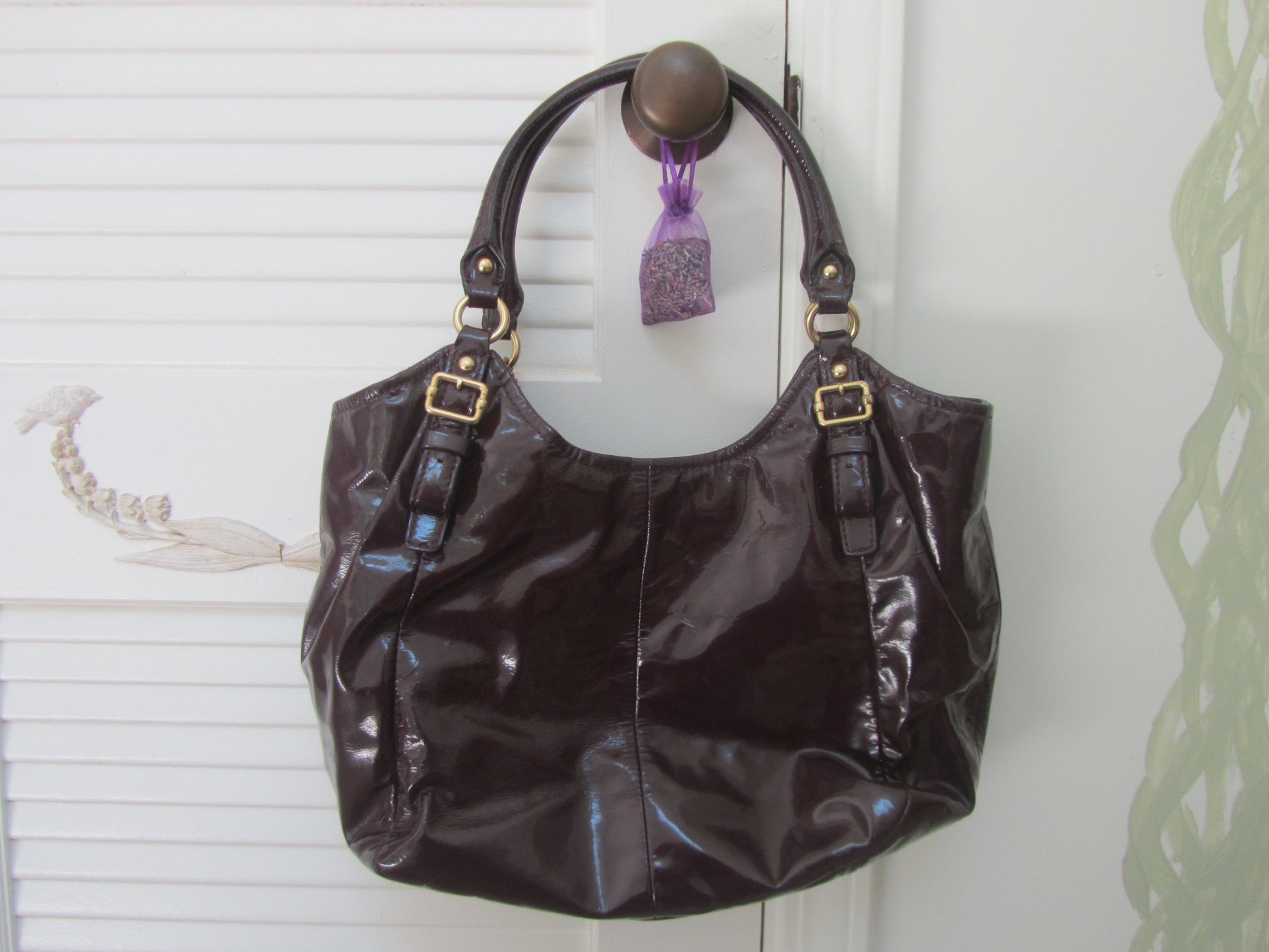 Brown handbag with gold accents hanging on a white door handle.